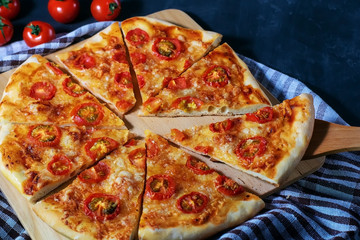 Freshly baked homemade pizza sliced in pieces lies on a black table