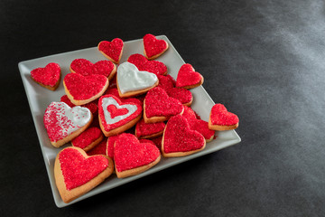 Obraz na płótnie Canvas Red and white heart shaped cookies on a white plate, symbol of love, black background with copy space