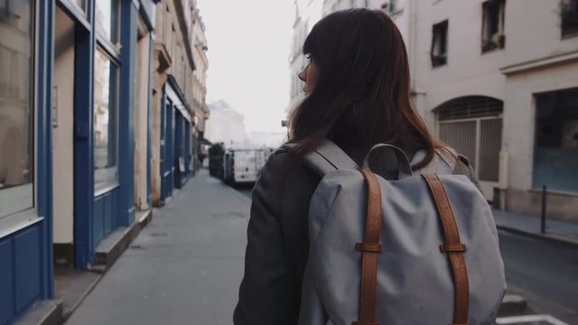 Camera follows beautiful female tourist with backpack walking along atmospheric autumn streets of Paris slow motion.
