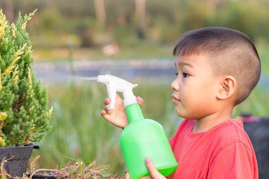 Soft​ focus. Portrait​ image​ of​ Asian​ little​ farmer​ child​ boy​ watering by bottle spray the​ flowers​ at​ the​ garden​ farm.​ 5 yeas old of child. Kids​ Learning​ and​ agriculture​ concept.