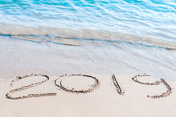 End of  2019 handwritten on the sandy beach with ocean wave washing away with water.. Happy new year 2020 concept.