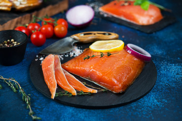 A piece of red smoked fish lies on a coal Board with spices.