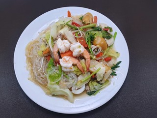 Thai food style, Top view of spicy vermicelli salad with seafood and mixed vegetable on white plate  isolated on black background, This food is most popular Thai food (Mung Bean Noodle Spicy Salad)