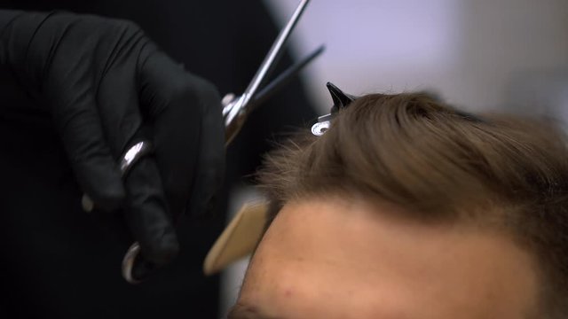 Client during beard shaving in barber shop. Hairdressing services. man cuts hair at a hairdresser-stylist in barbershop. scissors comb close-up Details of trimming. Cropped closeup  barber trimming