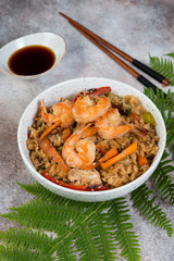 Tyahan with egg, vegetables and shrimp on a light concrete background with a fern leaf and soy sauce. Vertical photo.