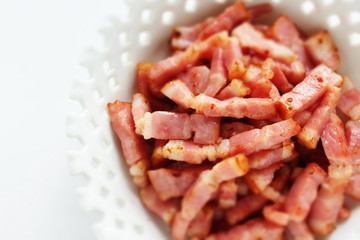 Fried bacon in white bowl on white background with copy space