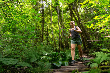 Naklejka na ściany i meble Adventurous Girl Trail Running in the Woods during a vibrant summer day. Taken in Deep Cove, North Vancouver, British Columbia, Canada.
