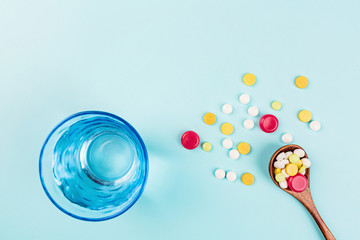 Colorful pills in wooden spoon and glass of water on a pastel blue background. Flat lay, top view, overhead, mockup, template. Pharmacy and medical concept