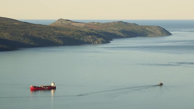 Beautiful seascape with bay and cape. Cargo ship on the roadstead and a vessel. Aerial view of the Staritsky Peninsula and the Sea of ​​Okhotsk. Nagaev Bay, Magadan Region, Far East Russia. Timelapse.