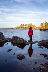 Wild Pacifc Trail, Ucluelet, Vancouver Island, BC, Canada. Girl Enjoyin the Beautiful View of the Rocky Ocean Coast during a colorful and vibrant morning sunrise.