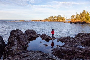 Fototapeta na wymiar Wild Pacifc Trail, Ucluelet, Vancouver Island, BC, Canada. Girl Enjoyin the Beautiful View of the Rocky Ocean Coast during a colorful and vibrant morning sunrise.