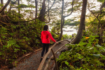 Naklejka na ściany i meble Adventurous Girl walking in a Forest with a beautiful view on the Ocean Coast during a vibrant colorful sunrise. Wild Pacifc Trail, Ucluelet, Vancouver Island, BC, Canada.