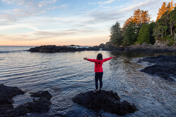 Fototapeta na wymiar Wild Pacifc Trail, Ucluelet, Vancouver Island, BC, Canada. Girl Enjoyin the Beautiful View of the Rocky Ocean Coast during a colorful and vibrant morning sunrise.