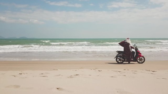 Santa Claus on the seashore rides a bike with a bag of gifts.