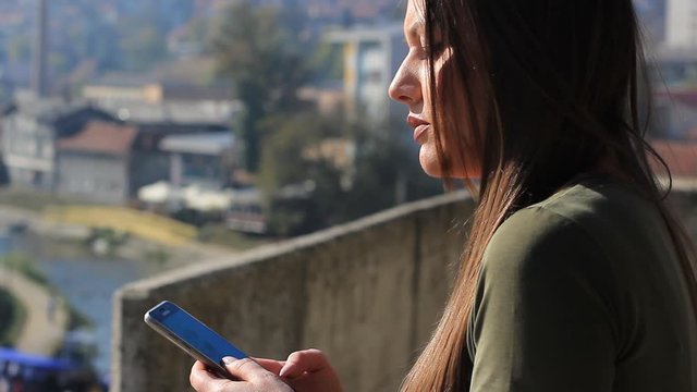Young unhappy brunette typing a message on the smartphone, on the bridge over the river. depression concept anxiety and suicidal thoughts