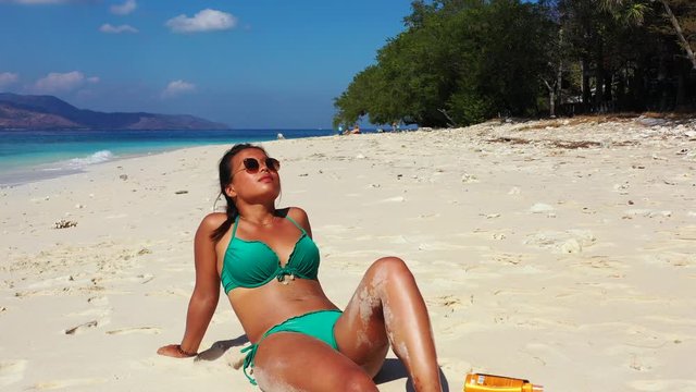 Close up, beautiful asian woman in the green bikini sunbathing on the tropical beach
