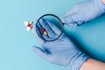 Concept - pharmaceutical testing, testing of medicines, magnifying glass, tablets on a blue...