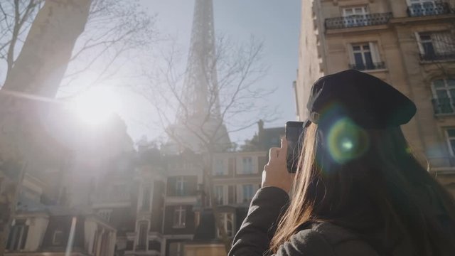 Happy beautiful tourist woman taking smartphone photo of Eiffel Tower on Paris vacation, amazing lens flare slow motion.