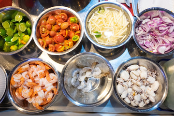 Top view of raw materials such as fresh shrimp, boiled shrimps, squids, onion, lemon in container of kitchen ingredient for cooking food.