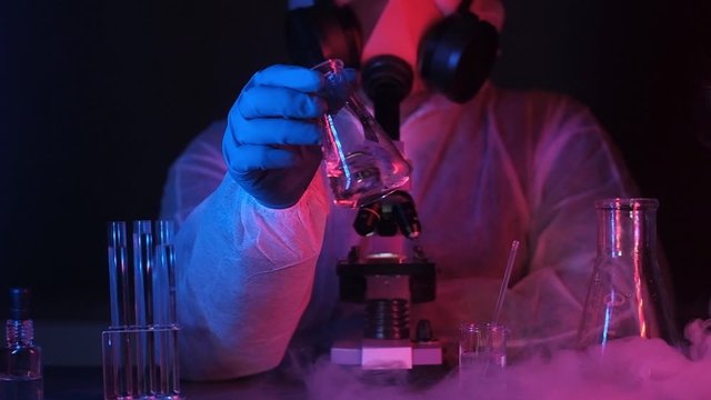 scientist biologist or chemist in laboratory neon light shakes transparent liquid in beaker.Liquid nitrogen floats on equipment table. laboratory experiments with cryogen and nitrogen. Lab equipment.