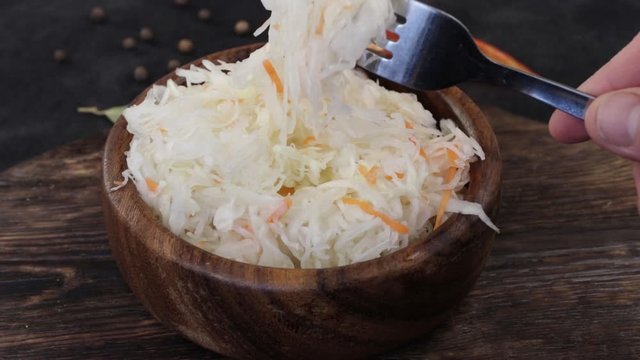 Hand with a fork takes tasty sauerkraut or fermented cabbage in a wooden bowl isolated on a wooden background. Fermented food. Ingredient for bigos.