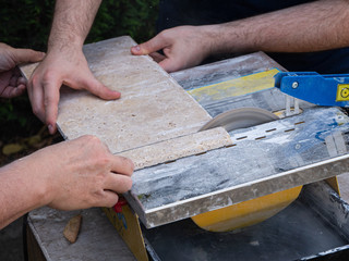 4 hands are cutting a travertine tile with a circular saw