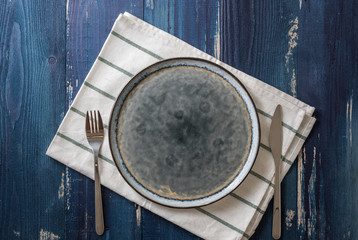Plate with utensils and dish towel on blue wooden background