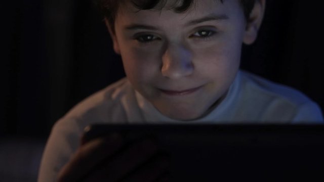 child in the evening watching cartoons or movies on the tablet in the evening in the bedroom. Browse the Internet before going to bed. Childhood with a tablet.