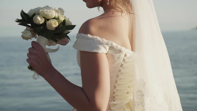 closeup young woman bride holding her wedding bouquet on sea background. concept femininity, celebration, flowers. white roses florist decoration. ceremony marriage