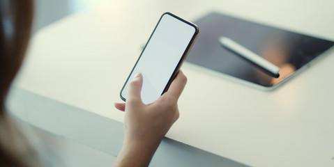Close-up view of young businesswoman using blank screen smartphone while working on the project