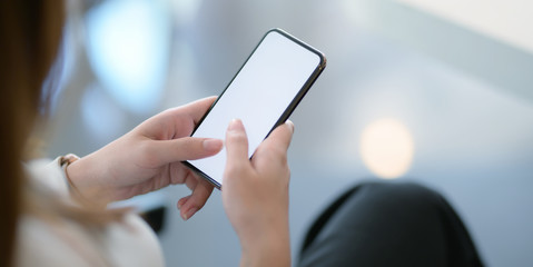Close-up view of young businesswoman using blank screen smartphone while working on the project in office