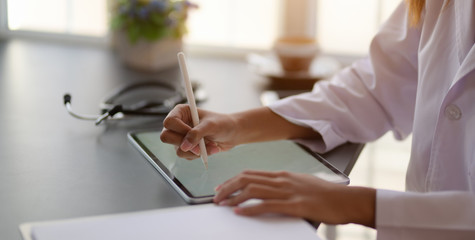 Cropped shot fo young female doctor working on medical records and exam results with tablet