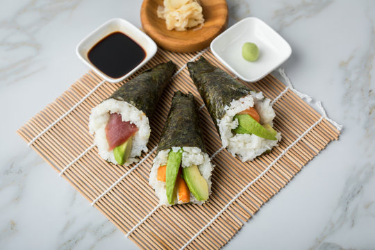 Lachs Fisch, Tunfisch und Surimi Avocado Temaki Sushi, eingelegter Ingwer mit Soja So&szlig;e und Sushimatte auf Marmor Hintergrund