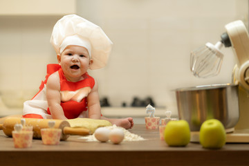 A Child, Baby, Girl, sits On The Kitchen Table, In A Cook's Cap