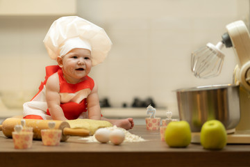 A Child, Baby, Girl, sits On The Kitchen Table, In A Cook's Cap