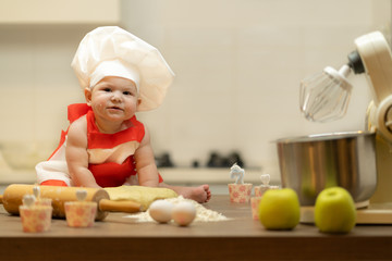 A Child, Baby, Girl, sits On The Kitchen Table, In A Cook's Cap