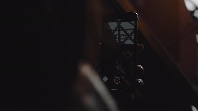 Close-up rear view female hand making smartphone video in glass tourist elevator moving up inside Paris Eiffel Tower.