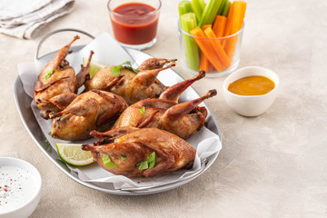 Tasty fried quail with herbs, celery, carrots and sauce on a light background.