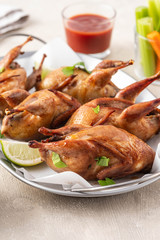 Tasty fried quail with herbs, celery, carrots and sauce on a light background.