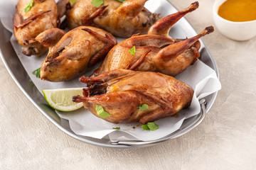 Tasty fried quail with herbs, celery, carrots and sauce on a light background.