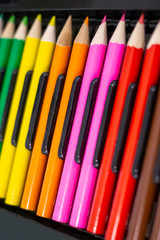 Set of bright wooden colored pencils laid out in a row with a dark background.