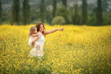 Fototapeta premium Happy family summer vacation. Mother with girl in rape field enjoying life at sunset. Pretty brunette with long healthy hair. Carefree girl over yellow field and blue sky. Countryside landscape