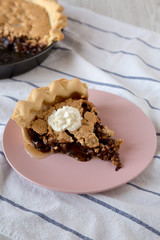 A piece of homemade Chocolate Walnut Derby Pie on a pink plate on a white wooden surface, low angle view. Closeup.