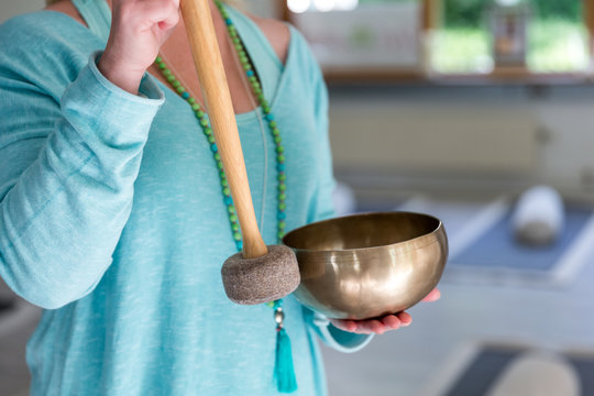 Frau schl&auml;gt mit Schlegel gegen eine Klangschale aus Messing