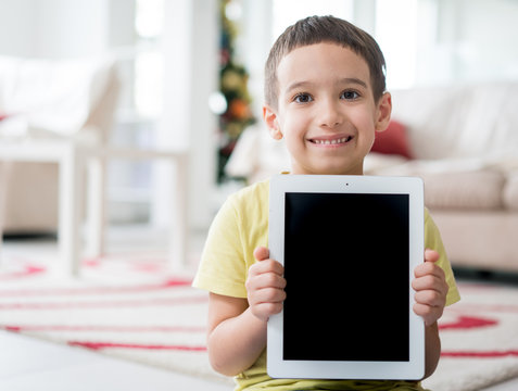 Little cute boy at home holding tablet with copy space