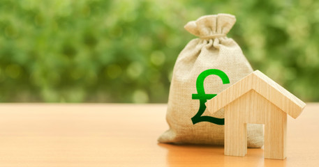 Wooden house figurine and money bag with pound sterling GBP symbol. Budget, subsidized funds....