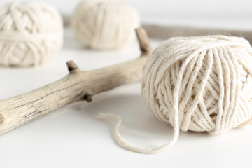 Balls of white yarn and rustic sticks on a white table. Threads of wool boho image.Good for macrame...