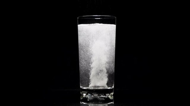 Close-up effervescent tablet aspirin in glass of water on a dark background.