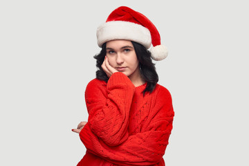 Sad brunette girl in a red sweater and Santa hat isolated over grey background.