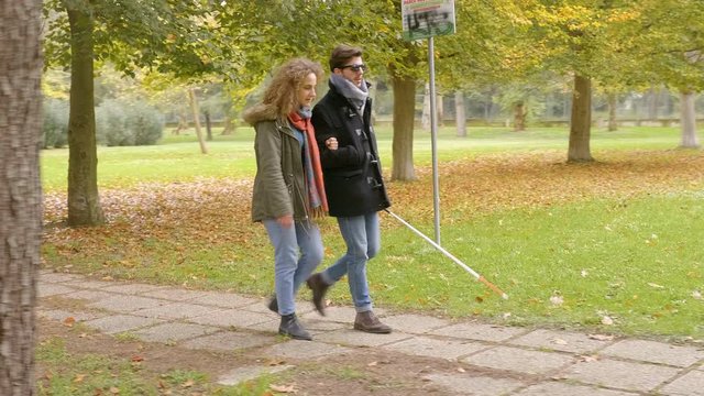 blind young man walking  at the park touching the ground with his girlfriend